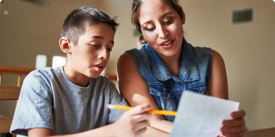 A parent helping her son with schoolwork at a table