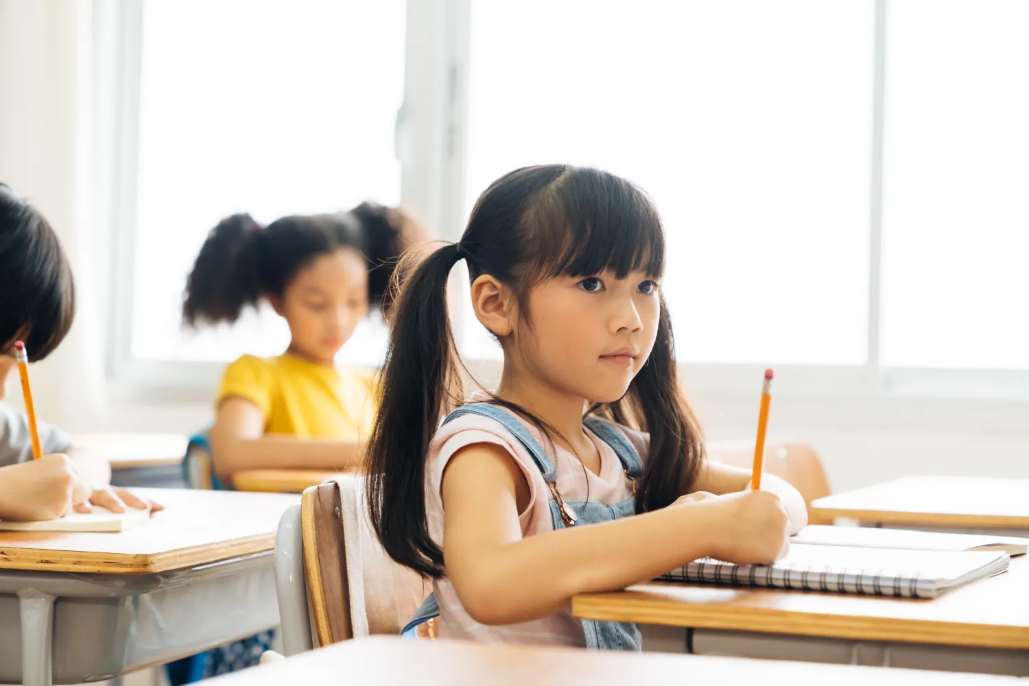 A young student writing at her desk in a classroom